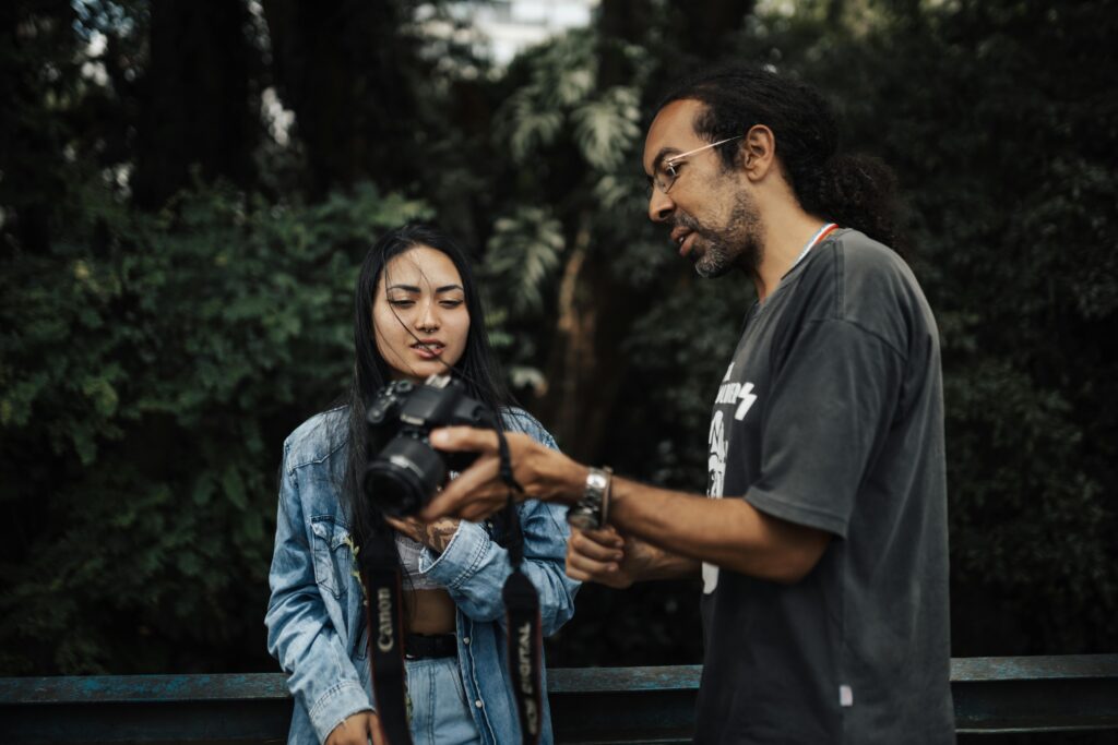 Two adults discussing photography with a Canon camera in a lush park setting.